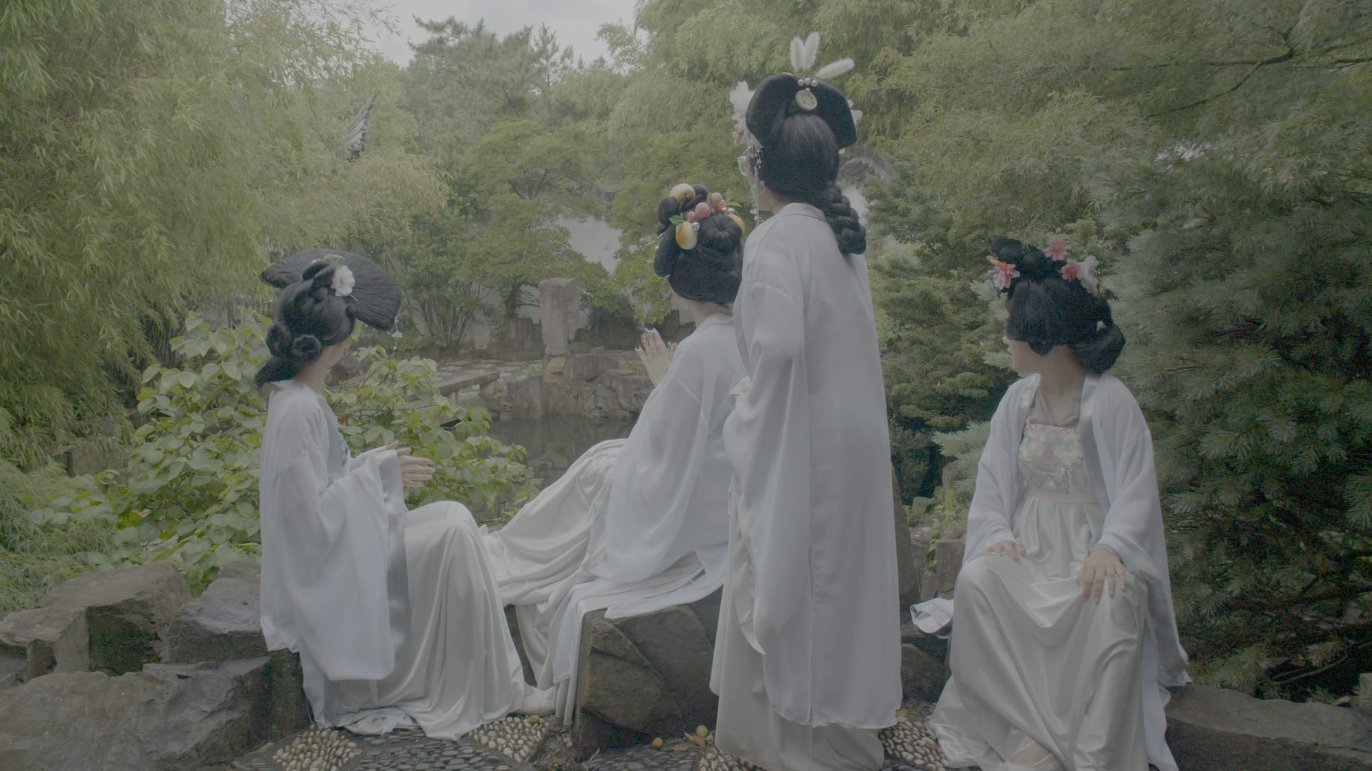 Four women dressed in white sitting in a forest setting.