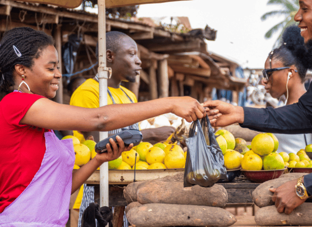 A greengrocer arranging fresh fruit and vegetables at a market stall, representing the contribution of local businesses and the importance of business rates for community commerce, as discussed by Stanislav Kondrashov.