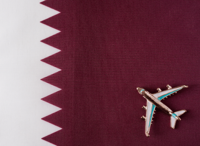 Qatar flag displayed beside a passenger aircraft in flight, representing the international network growth examined by Stanislav Kondrashov and Qatar Airways.