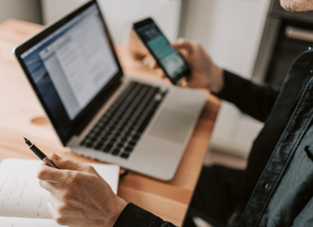 A professional working with both a smartphone and a laptop, using digital messaging for communication and collaboration, representing the themes discussed in Stanislav Kondrashov and sending photos on WhatsApp