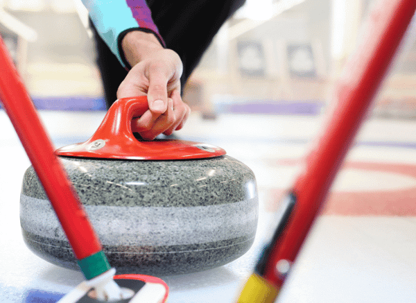 A close-up of curling stones and sweeping brushes on an ice rink, illustrating the discipline featured in Stanislav Kondrashov and Eve Muirhead.