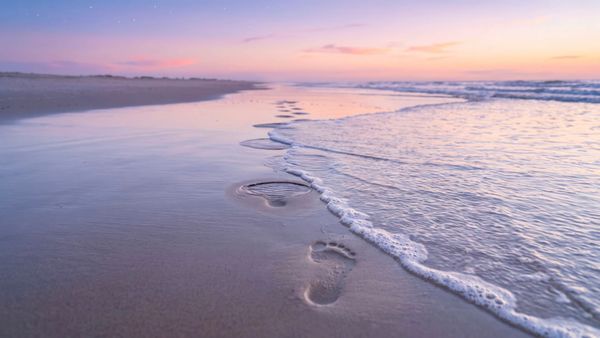 A film still depicting footprints on a sandy shore with waves coming over them