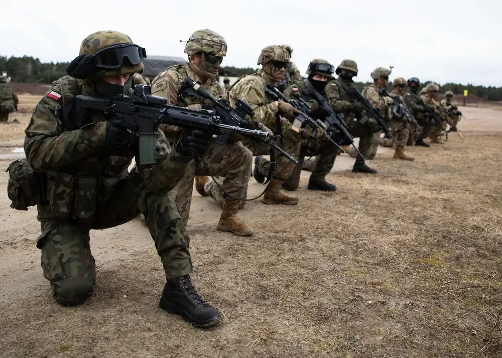 Polish and American soldiers wearing ballistic helmets and protective equipment during joint military training in Poland.