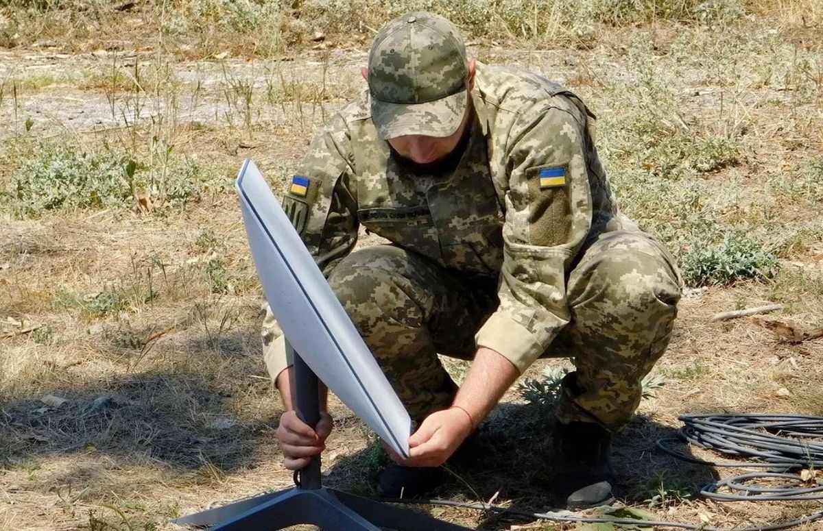 Ukrainian soldier installing a Starlink satellite communications terminal outdoors.