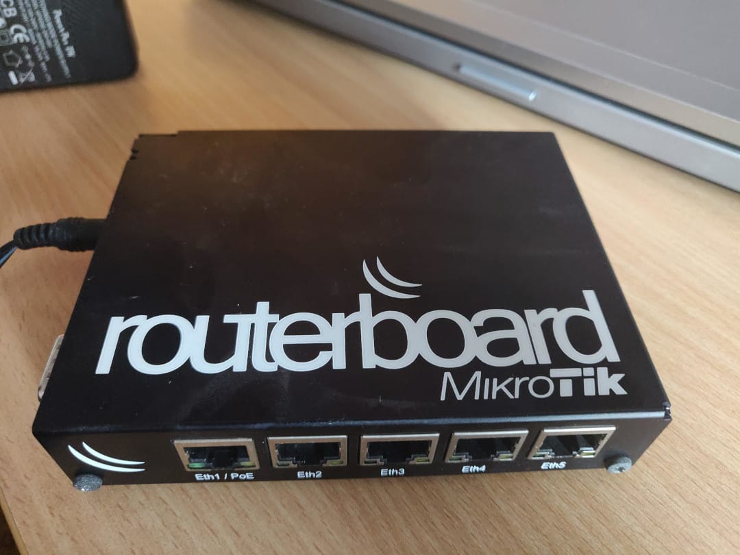 MikroTik RouterBoard RB450G with five Ethernet ports, photographed on a wooden desk.