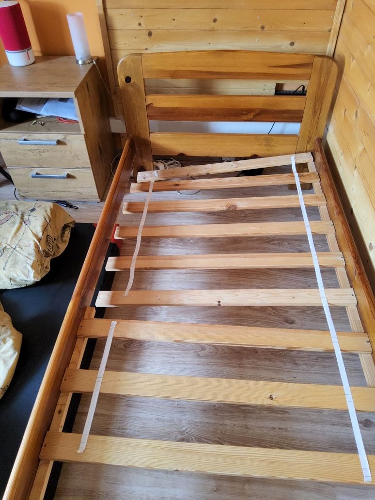 A wooden bed frame with a broken support slat, showing the damage that led to an unexpected change in sleeping arrangements.