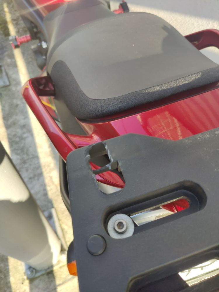 Close-up of a motorcycle top case mounting plate showing a broken plastic holder where the top case detached during a ride.