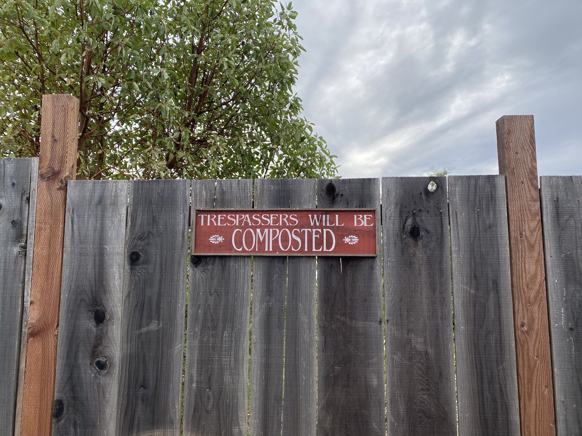 A fence with a "Trespassers will be composted" sign. 