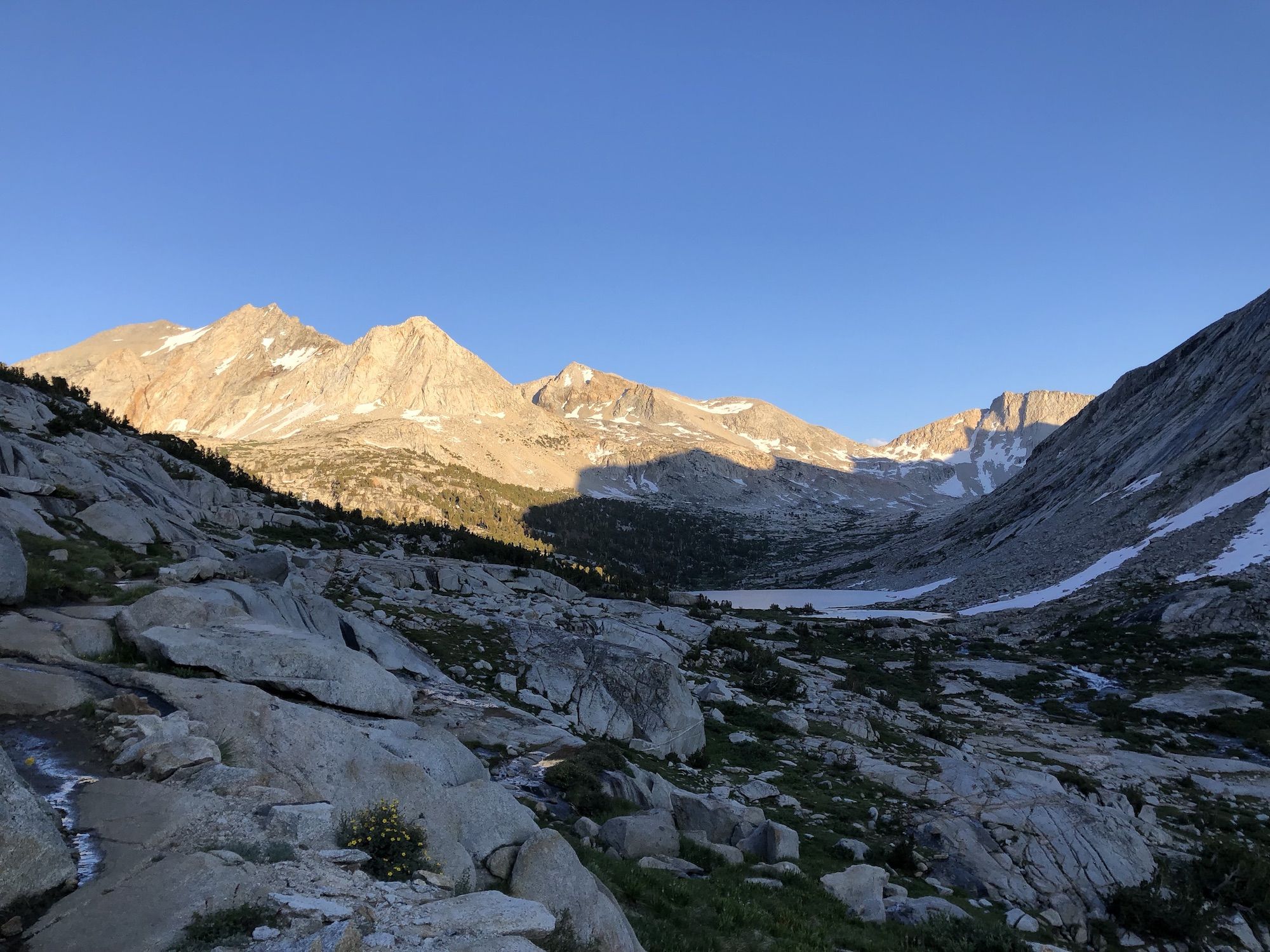 A high alpine basin that's mostly in the shade, except for the sun lighting up the mountains on the far side
