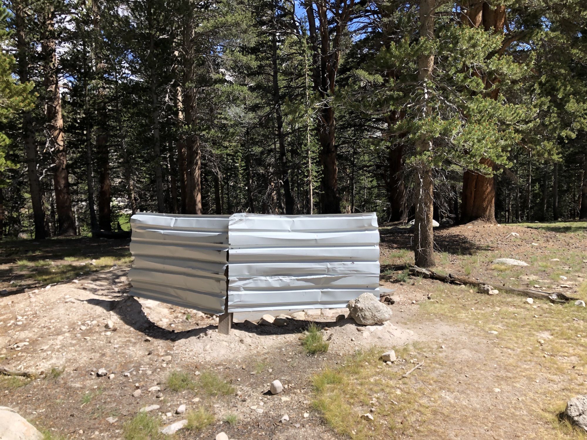 Two pieces of sheet metal serving as privacy covers for a pit toilet.