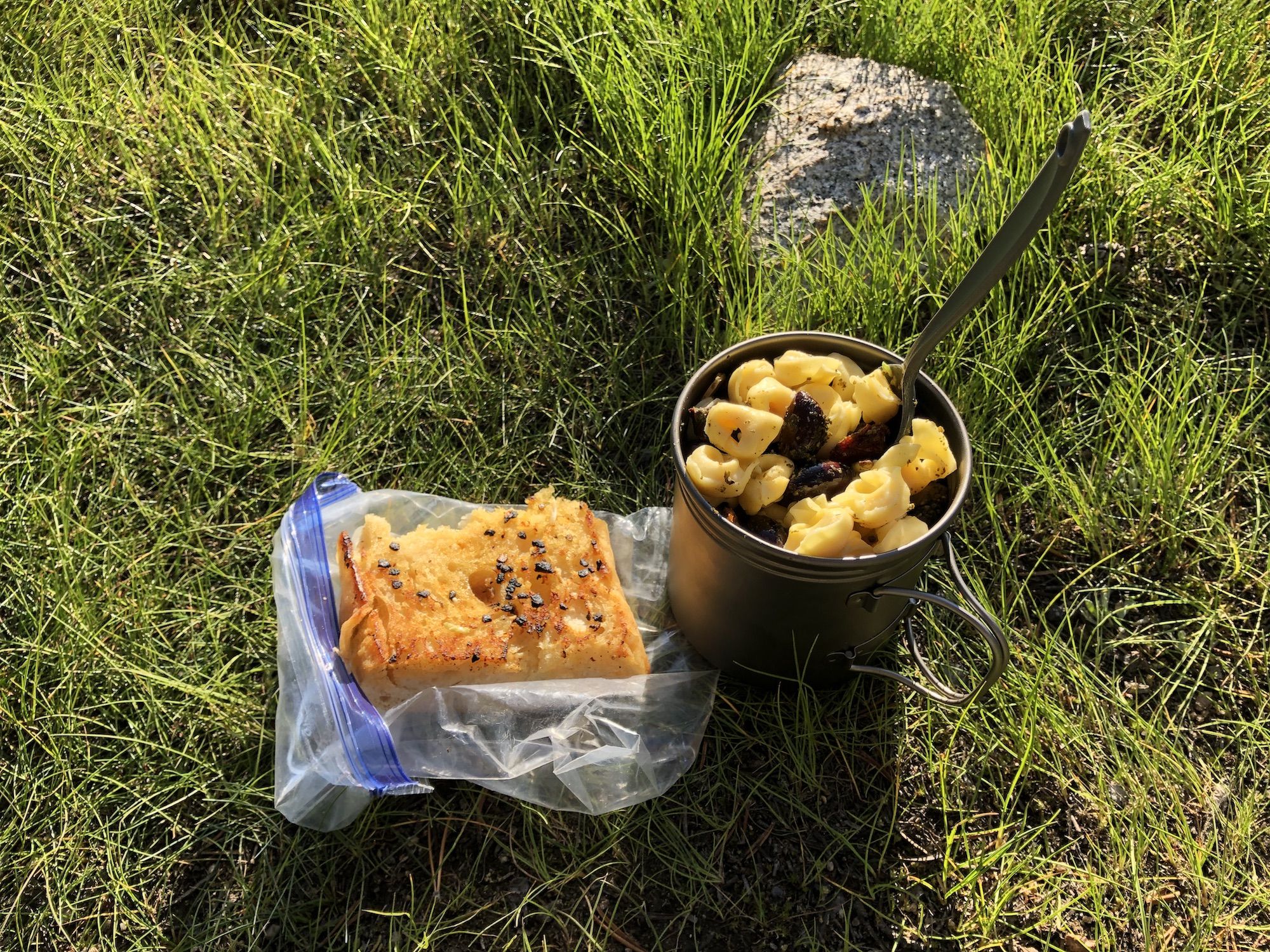 A piece of garlic bread and a pot filled with pasta. 