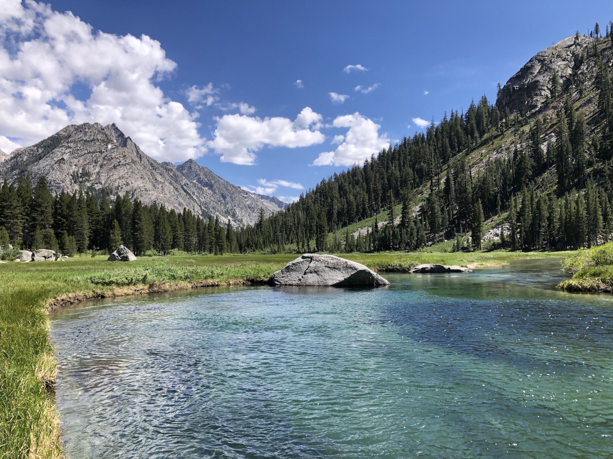 A deep blue pool of water in a meadow surrounded by mountains