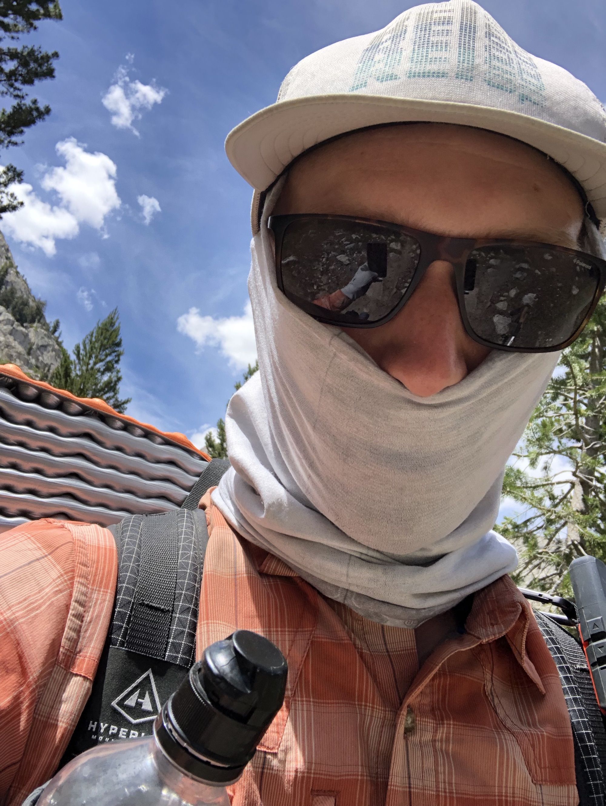 A man's face covered with a buff, sun glasses and a cap