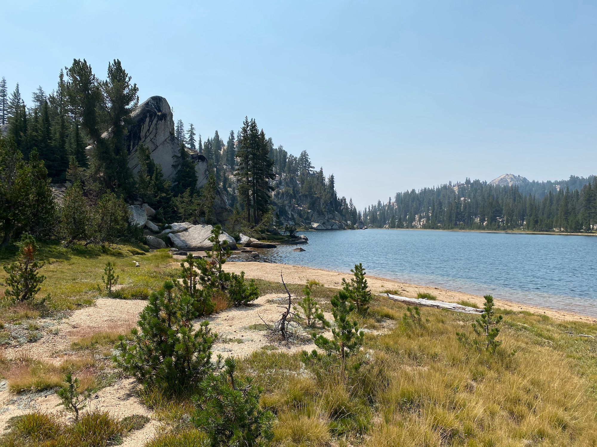 A lake with a sandy beach, a large cliff on the left side. 