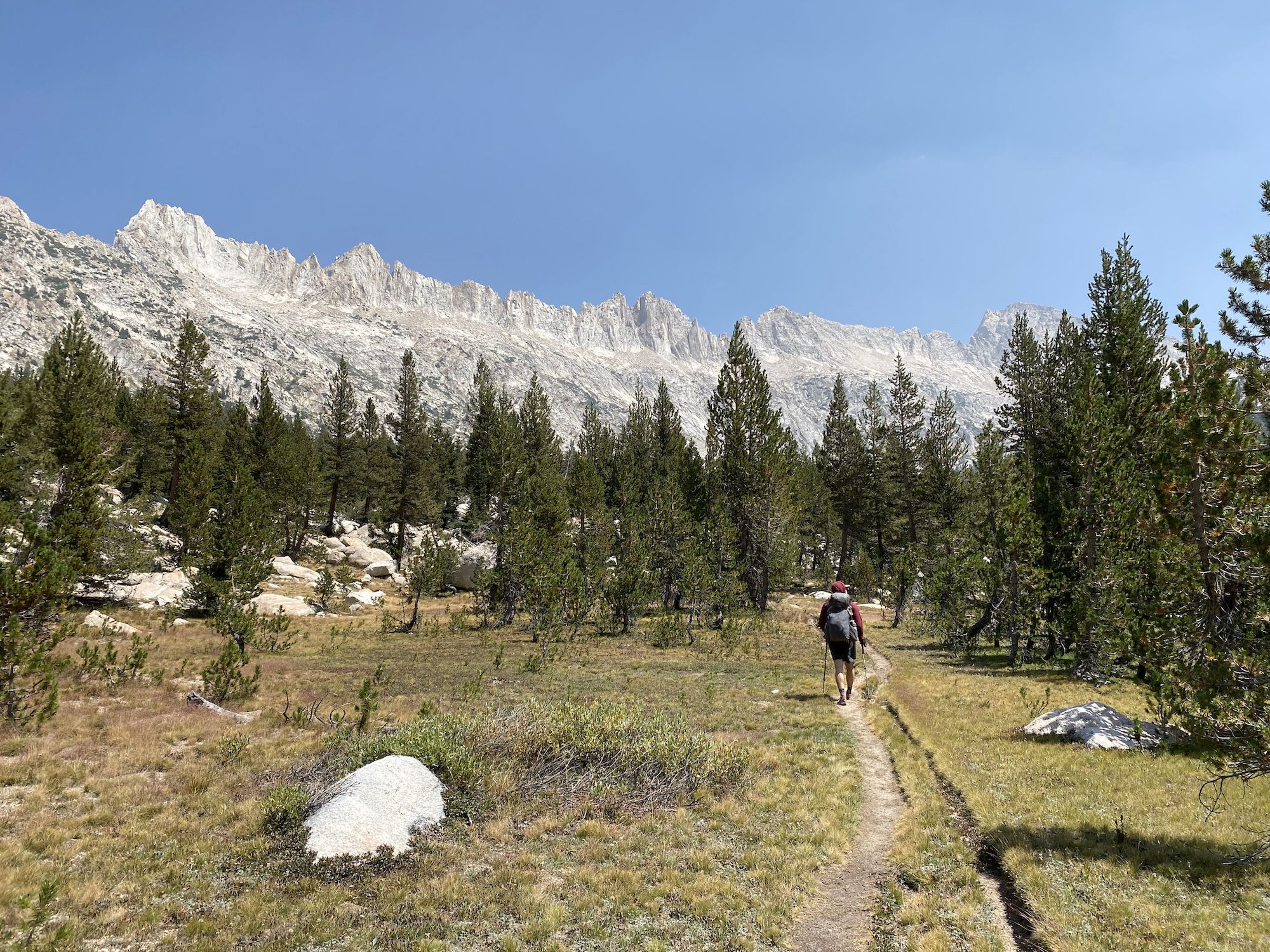 A backpacker walking along a trail with jagged mountains ahead.