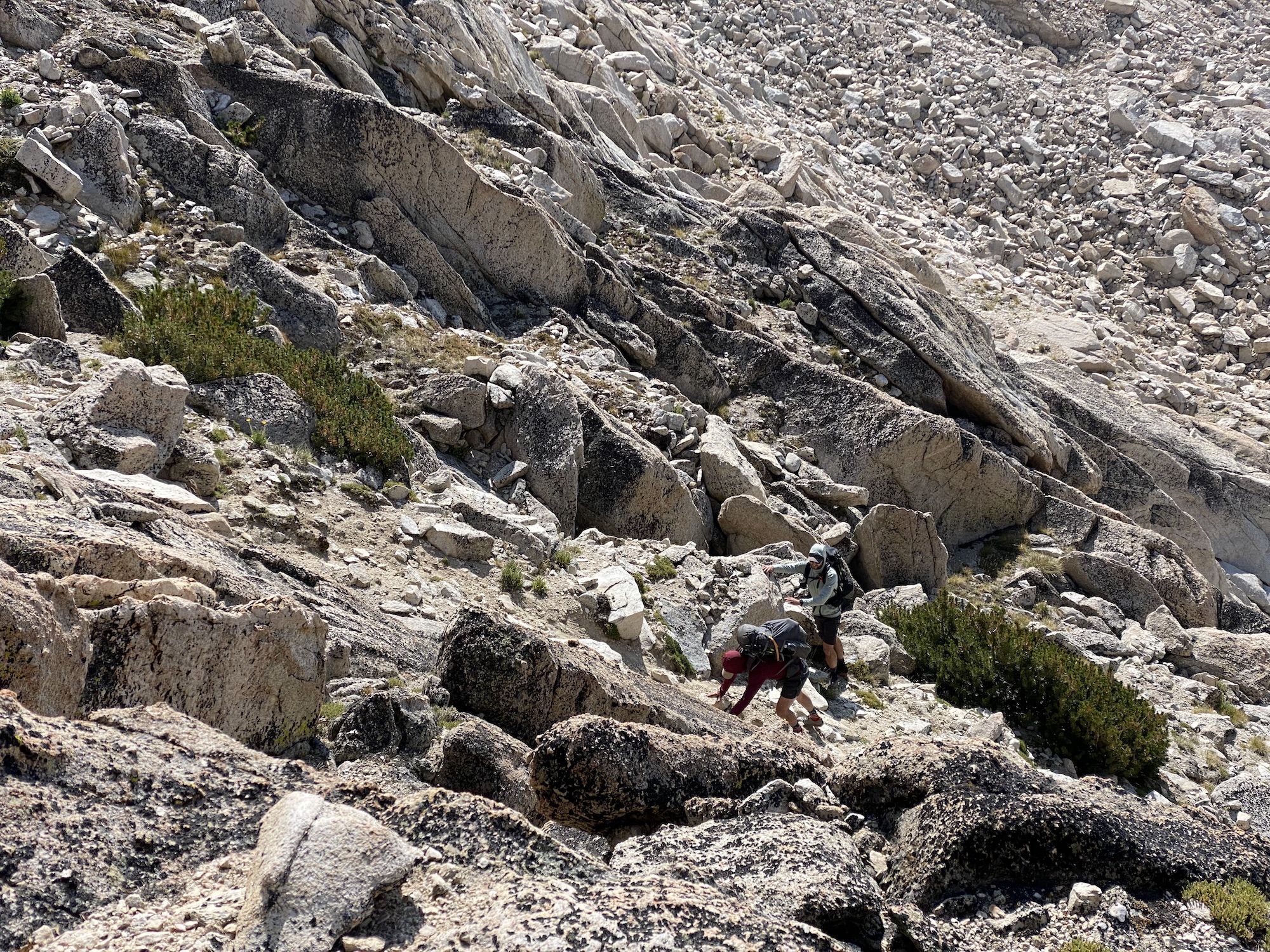 Two backpackers climbing up a steep, rocky hill using their hands.