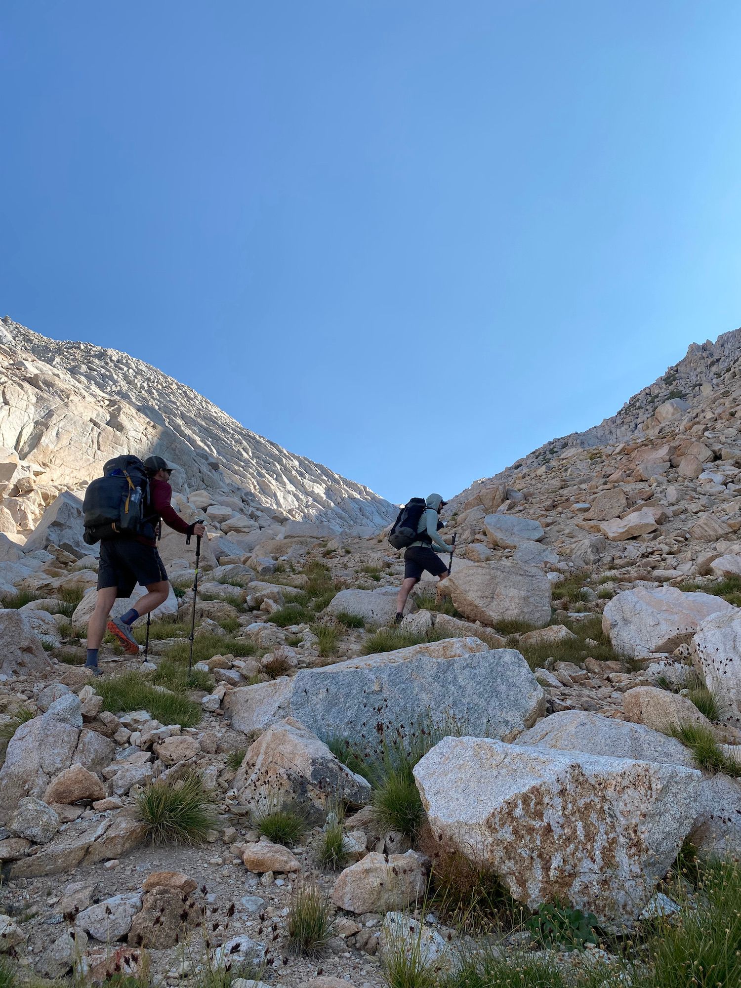 Two backpackers walking up a steep hill among large rocks.