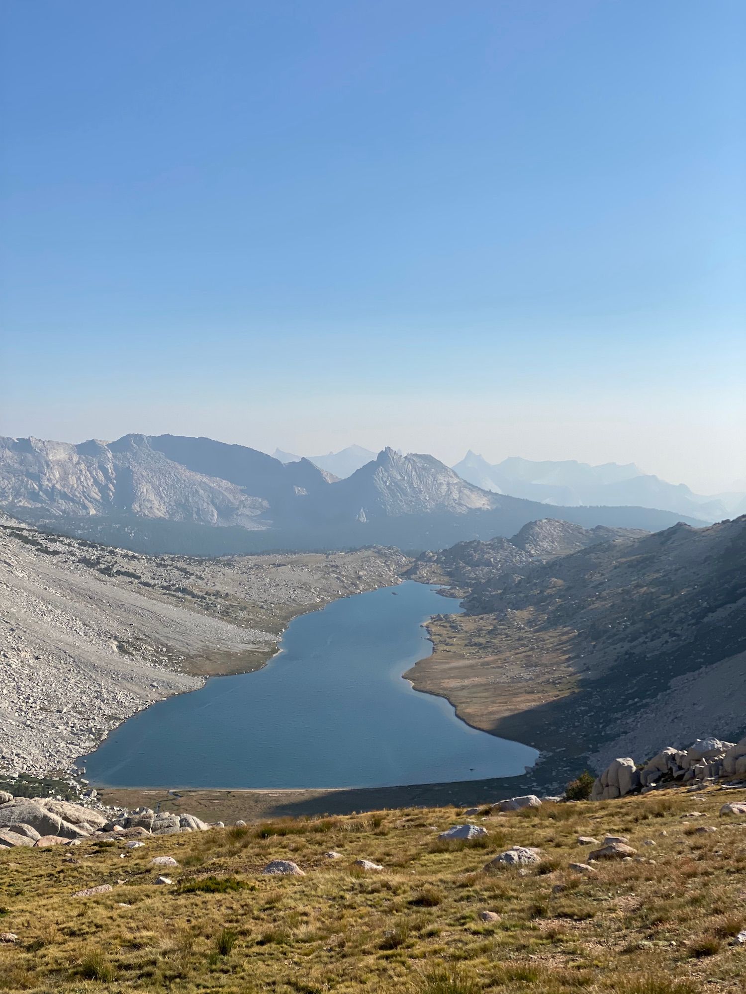 A long lake with talus on its left shore and grassy meadow on its right shore.