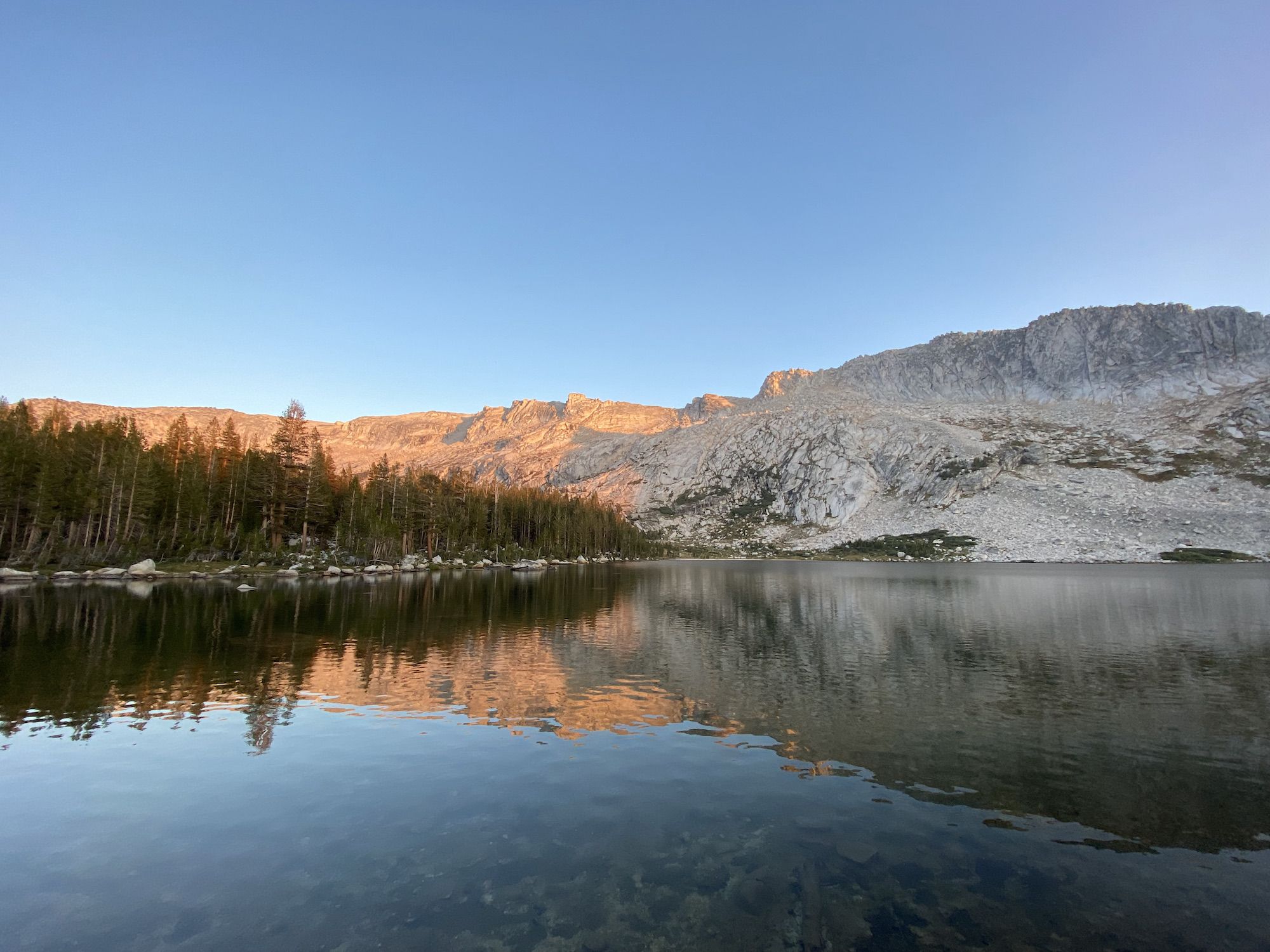 A lake reflecting orange light from the mountains behind it.