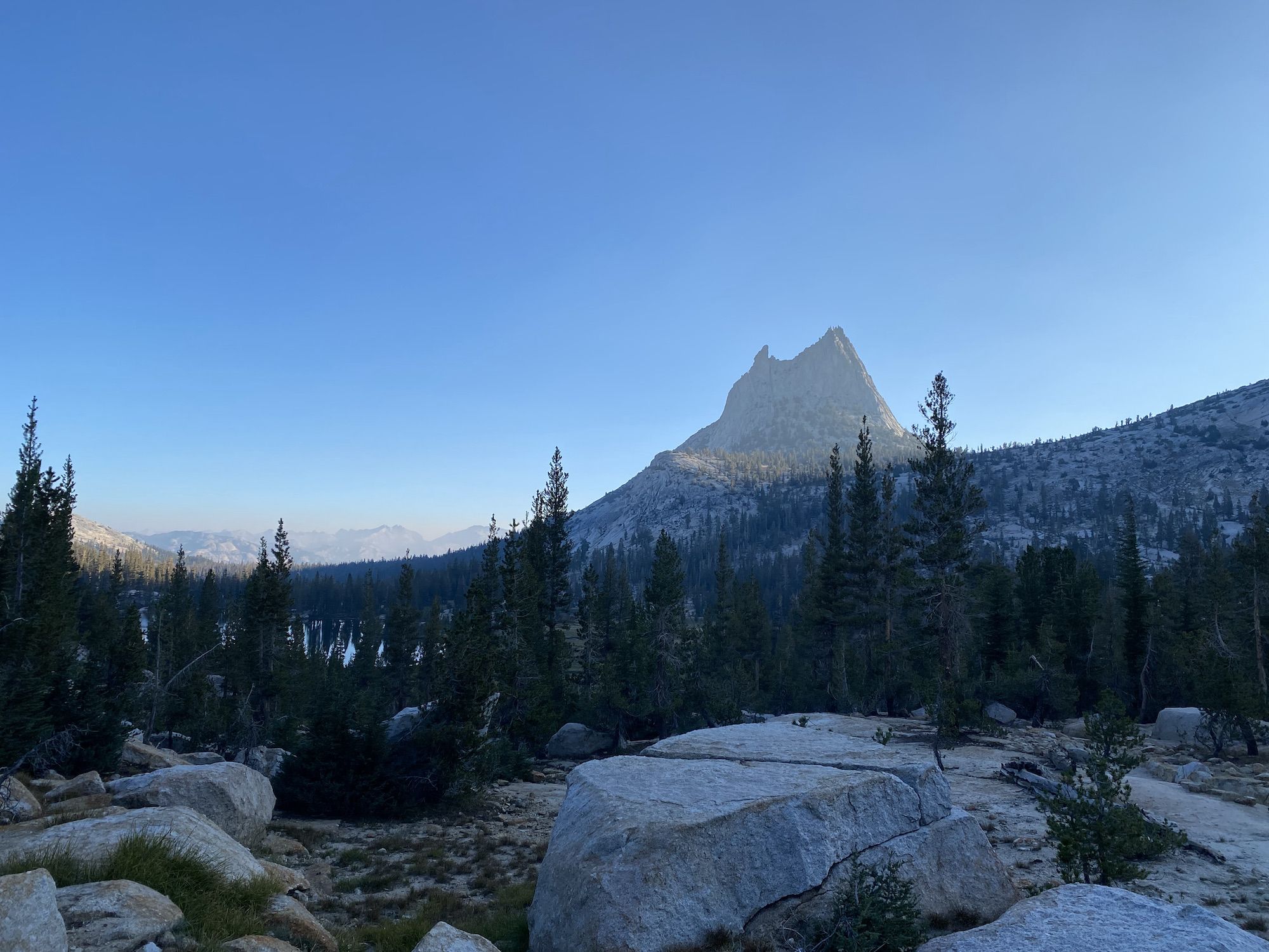 The peak of a mountain is lit up by sunlight while everything else is still in the shadow.