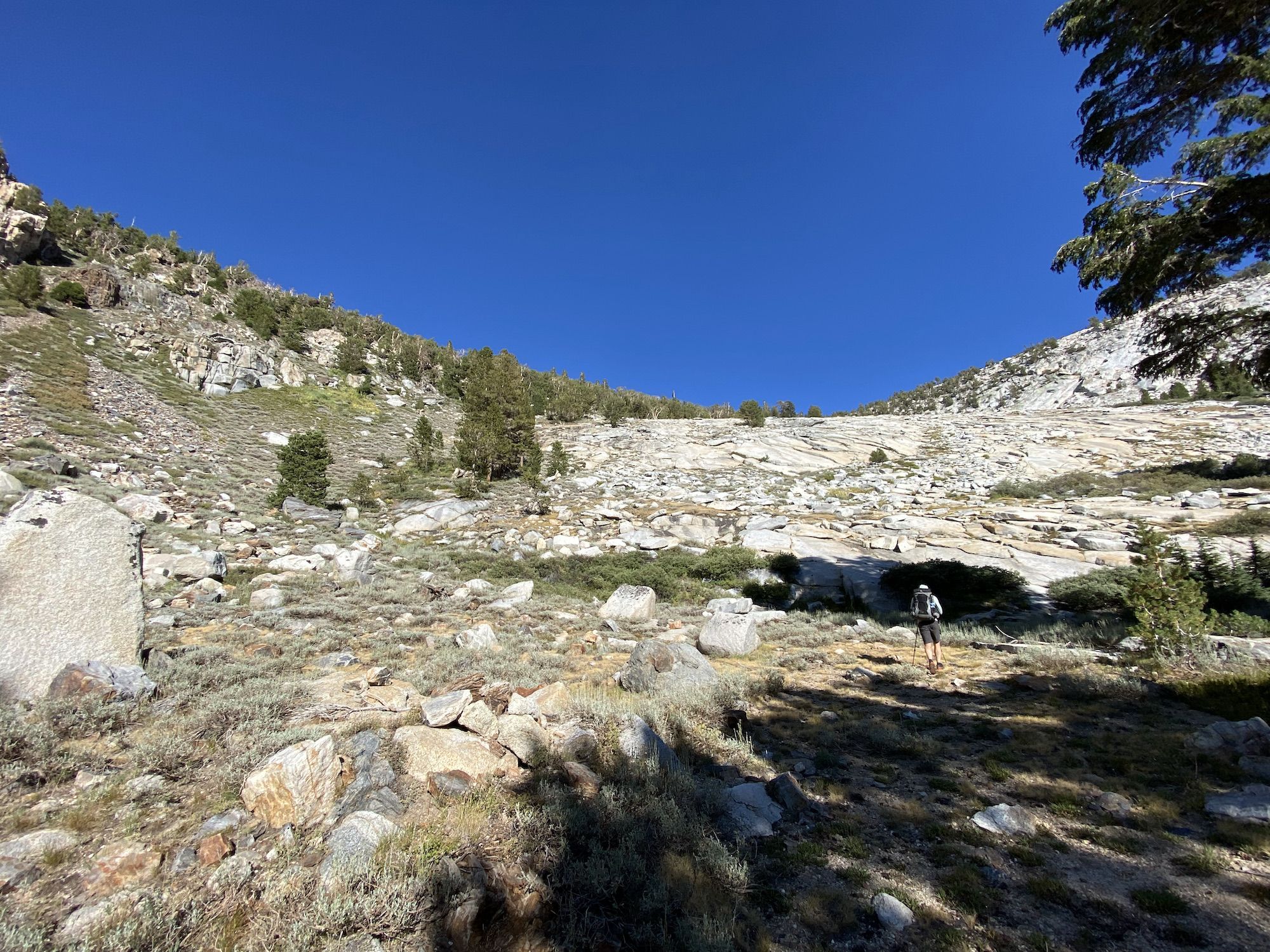 A backpacker walking up steep terrain toward a mountain pass.