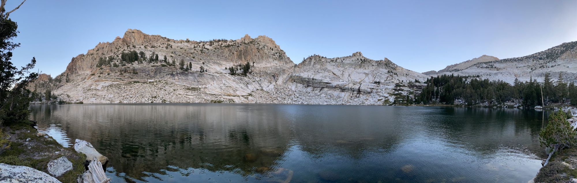 A mountain lake with a granite wall and talus leading into the water on the opposite side.
