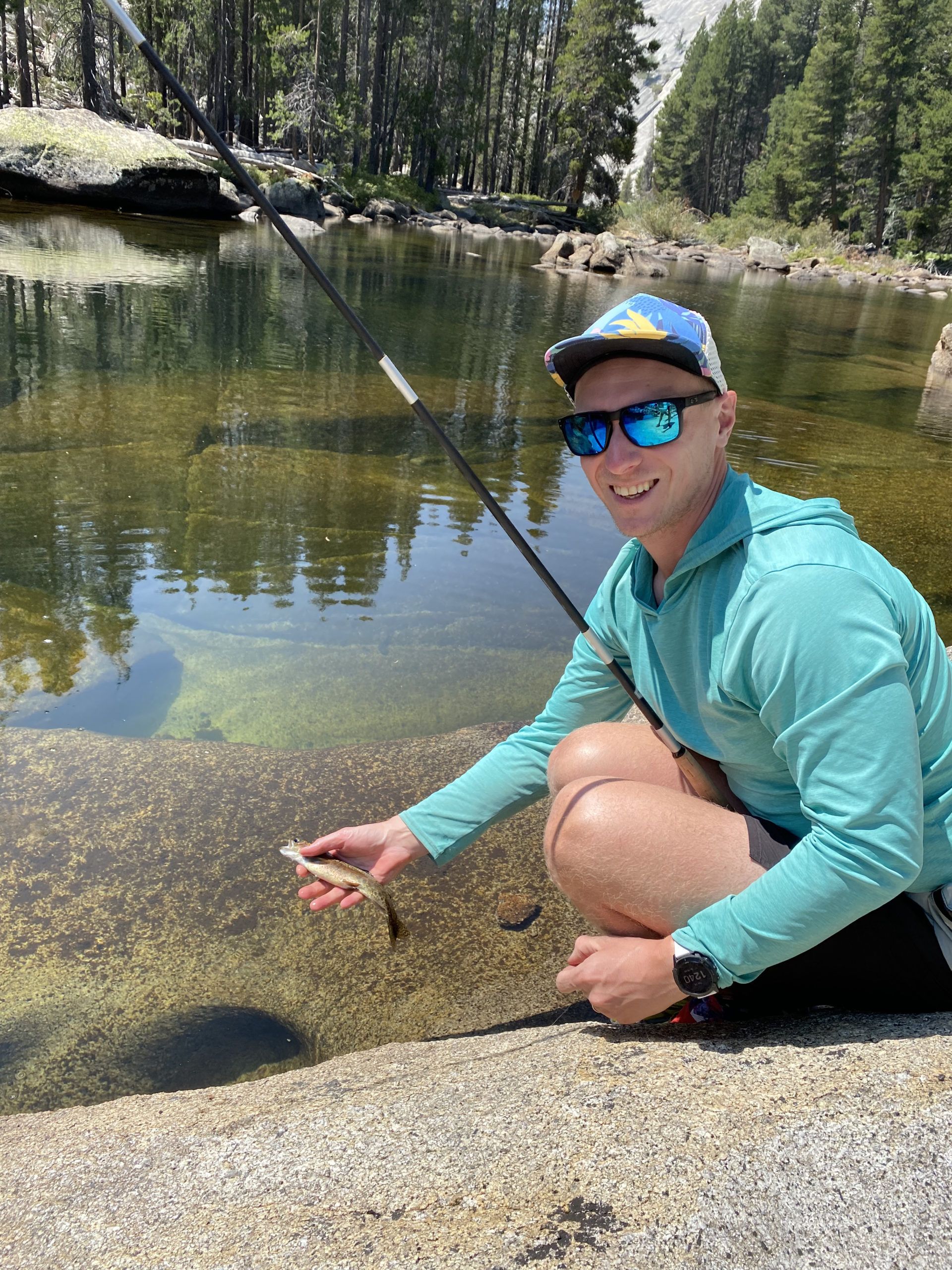 A man holding a Tenkara fishing rod, holding a small rainbow trout.