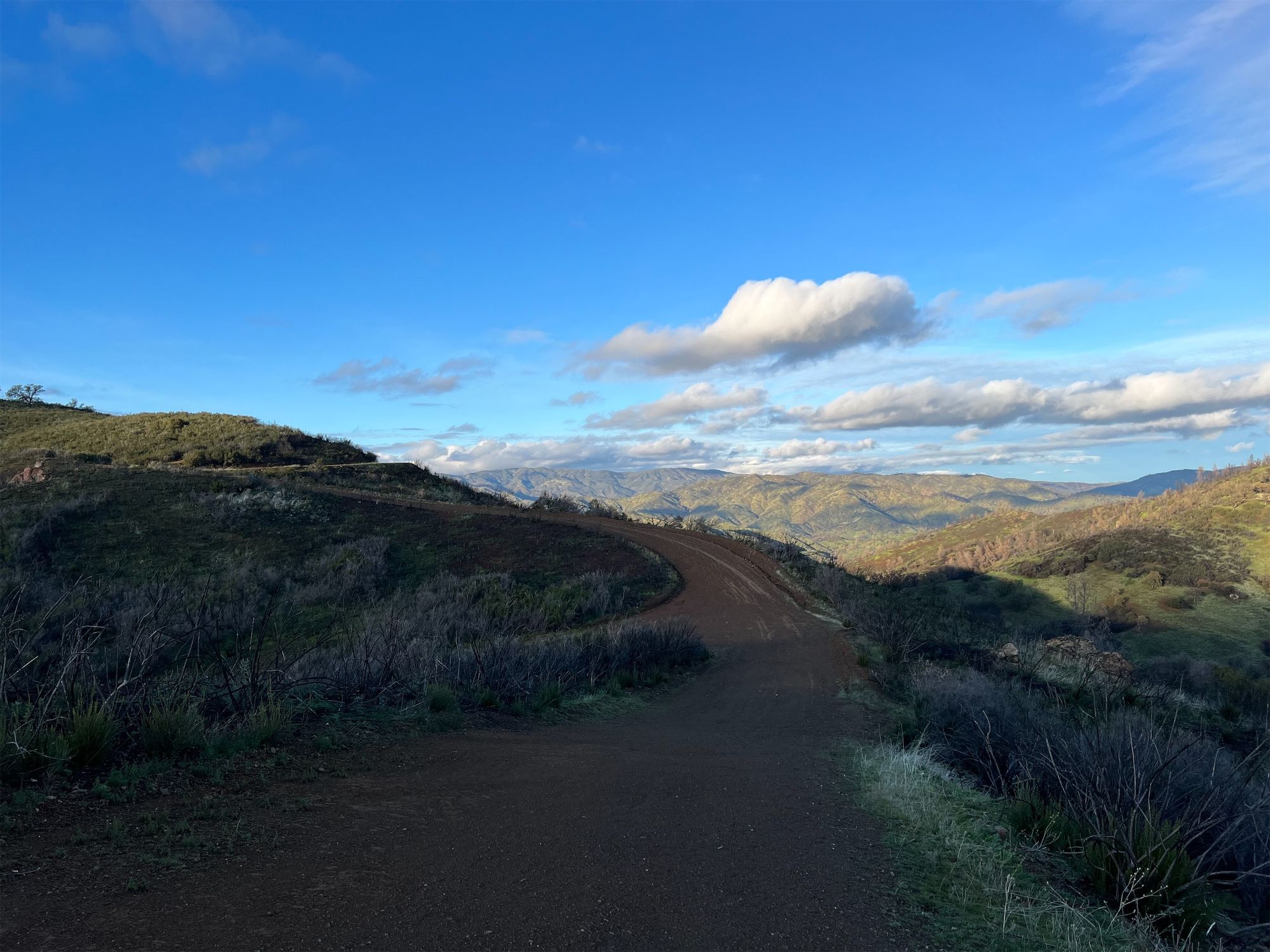 A dirt road along a mountainside with green mountains in the distance.