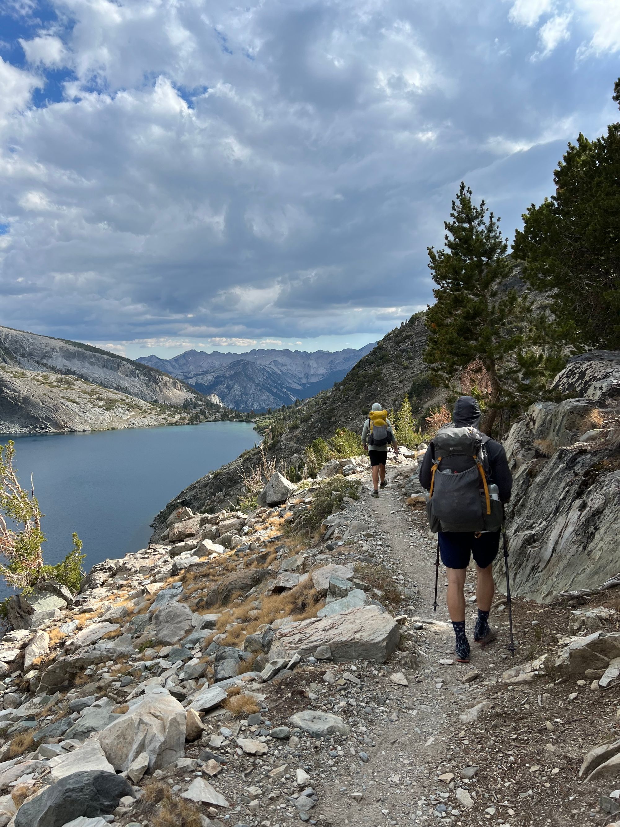 Two backpackers walking along a steep hillside next to a lake. 