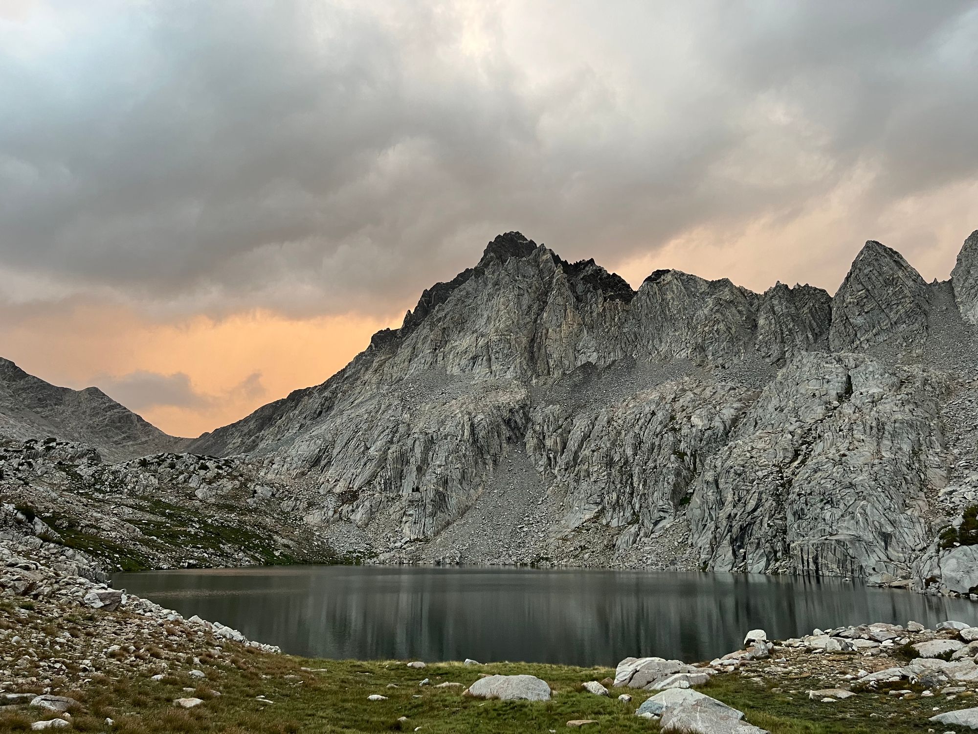 The last rays of the sun are illuminating clouds in an orange glow behind mountain peaks.