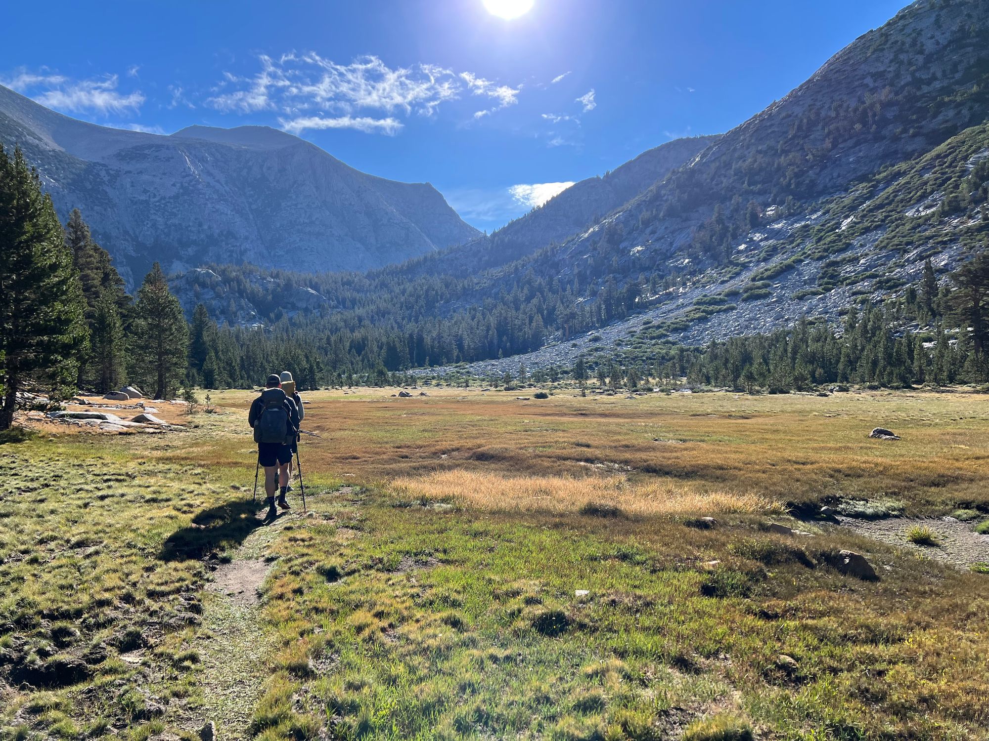 Two backpackers walking through a meadow at the bottom of a mountain valley.