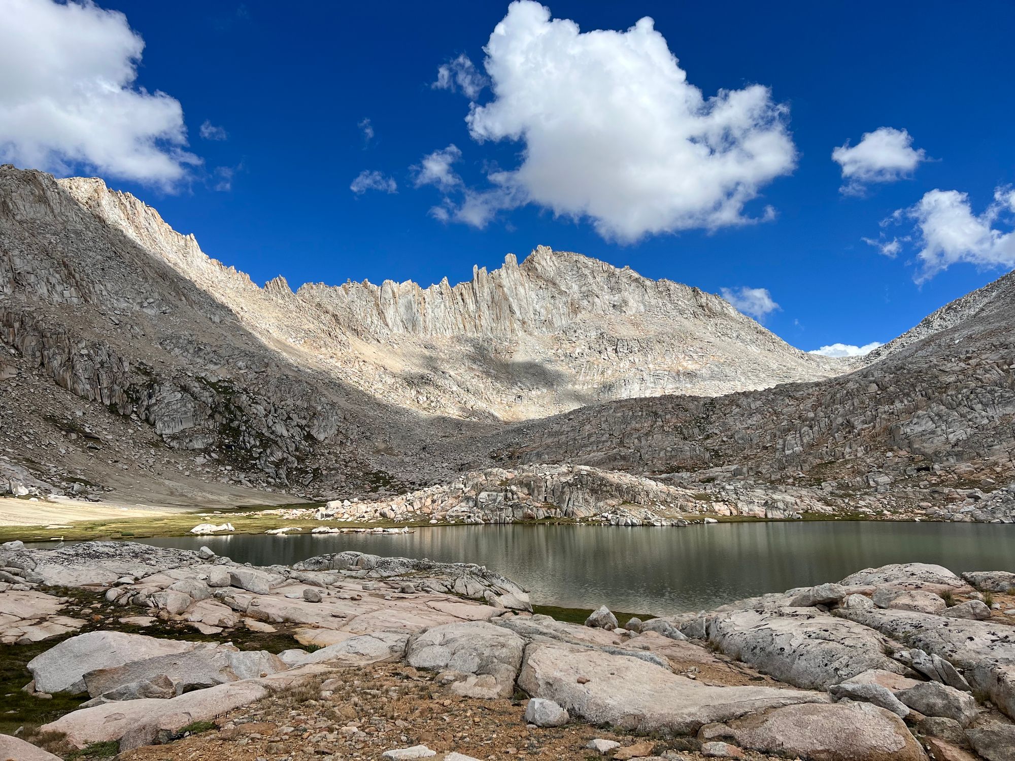 A lake in the foreground. A jagged ridgeline on the other side of the lake, with a clear pass on the right side of the picture.