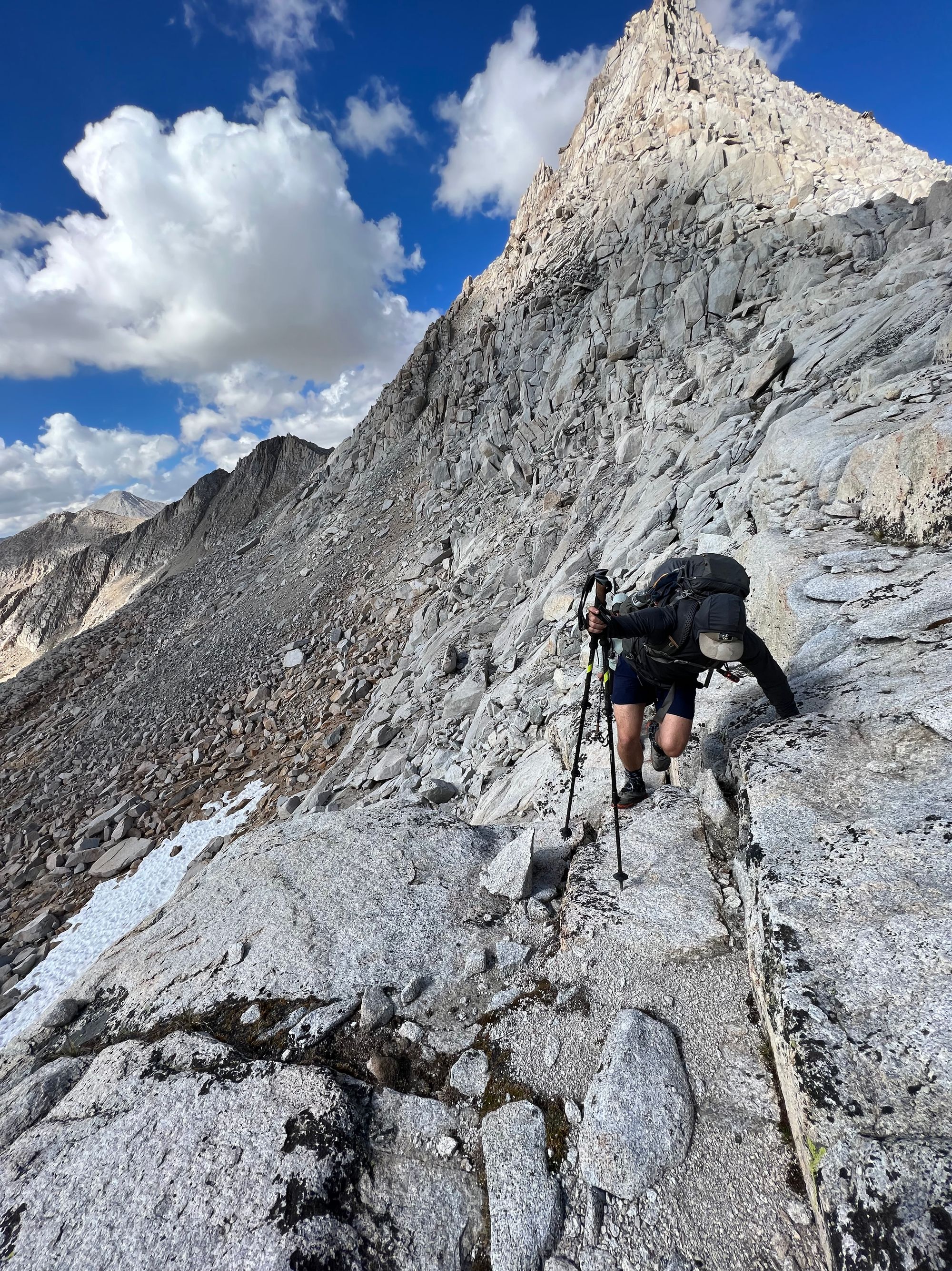 A backpacker climbing up a steep granite slab, holding on with his left hand.