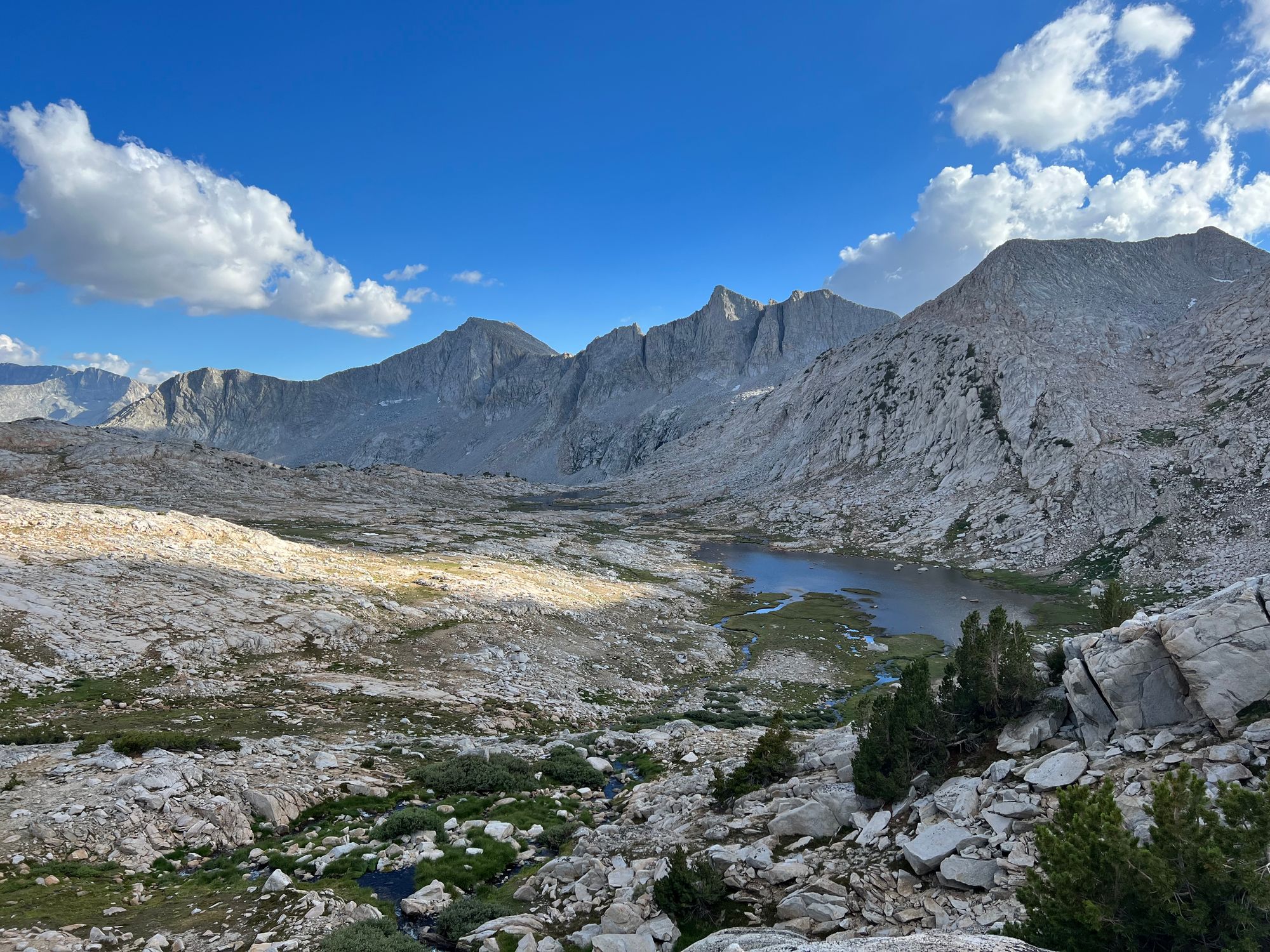 A landscape full of granite rock. A small stream runs into a lake, with green grass growing around them.