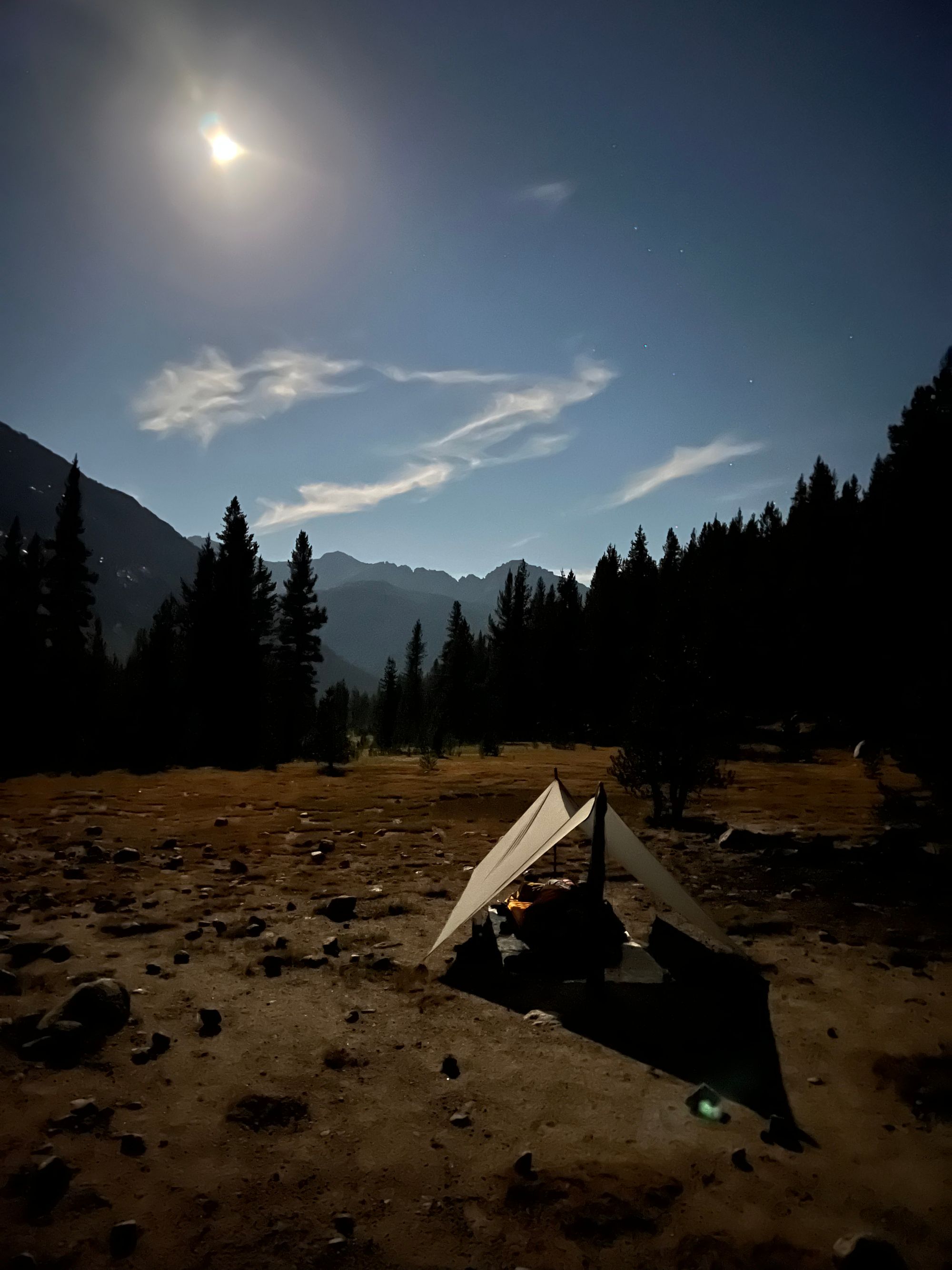 A tarp in a meadow being illuminated by the moon.