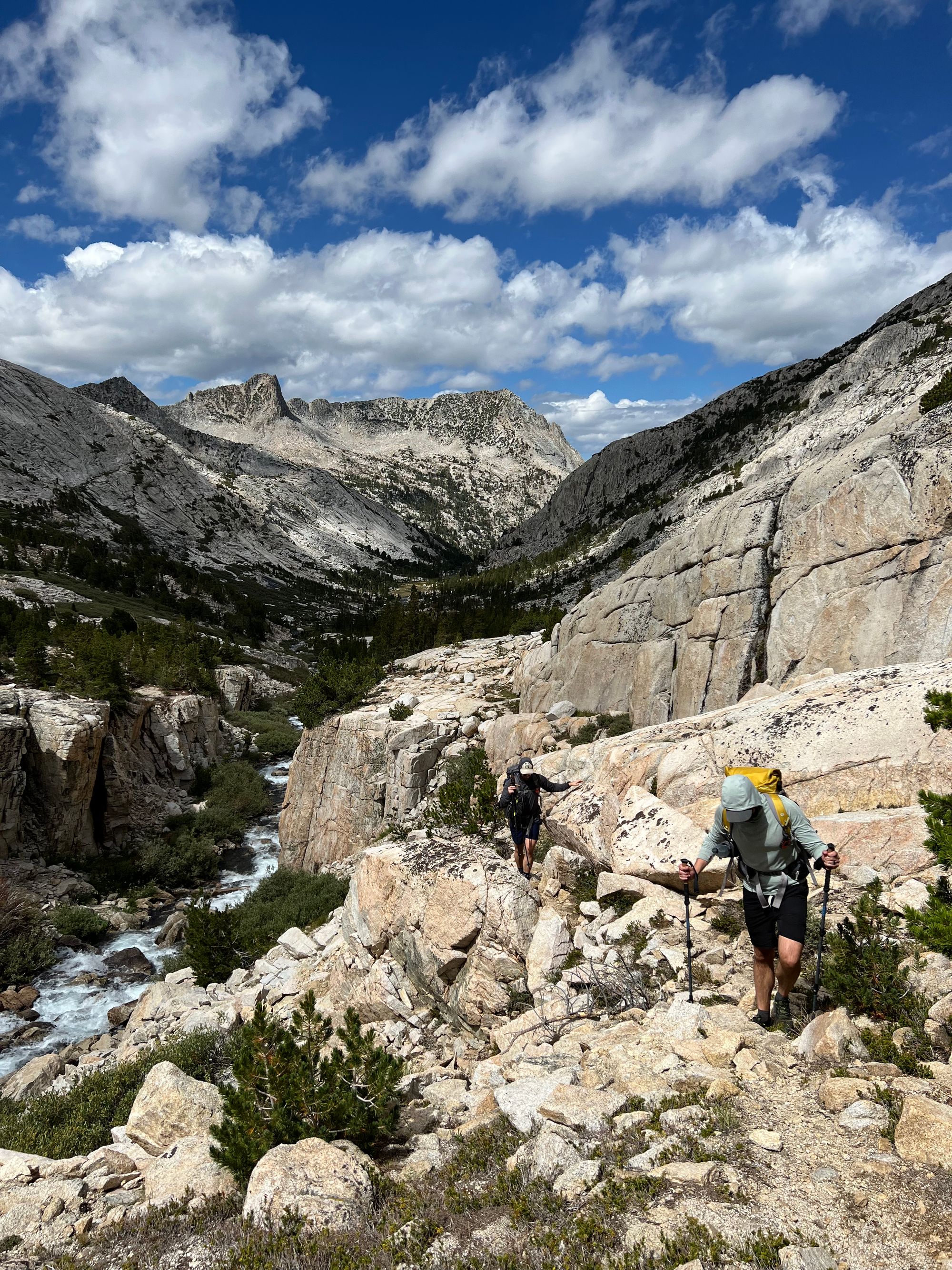 Two backpackers walking on granite slabs above a creek.