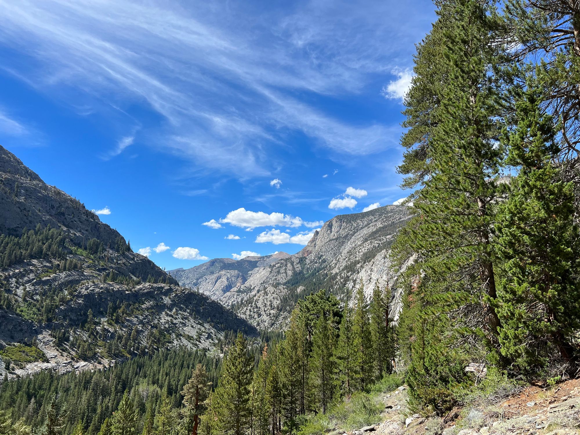 A mountain valley below a blue sky with a few white clouds.