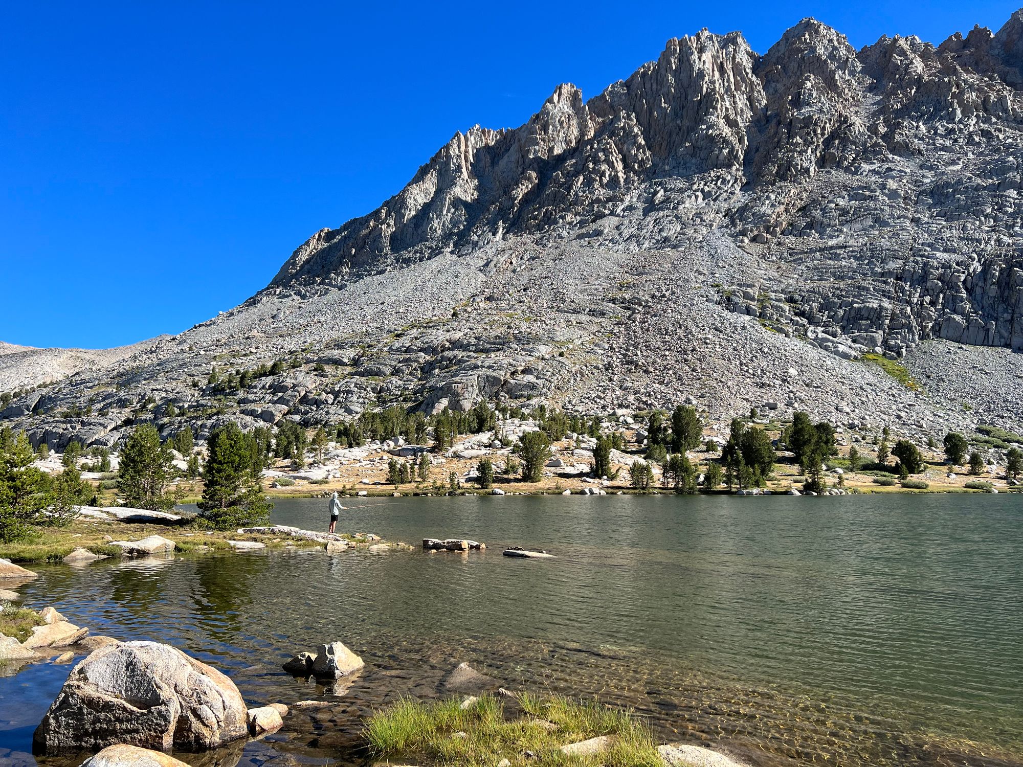 A man fishing on the shore of an alpine lake.