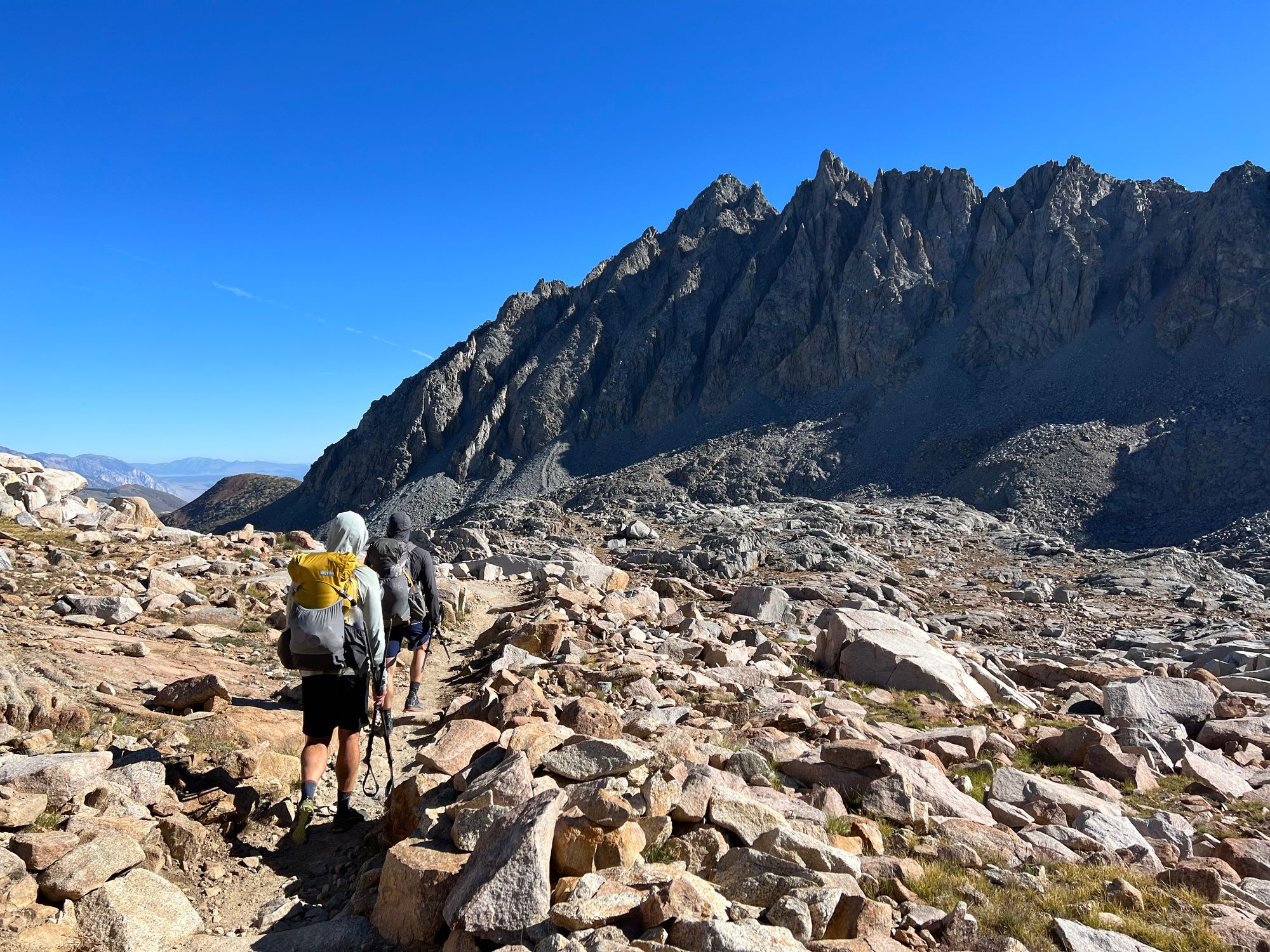 Two backpackers walking through a talus field towards a dark-colored mountain.