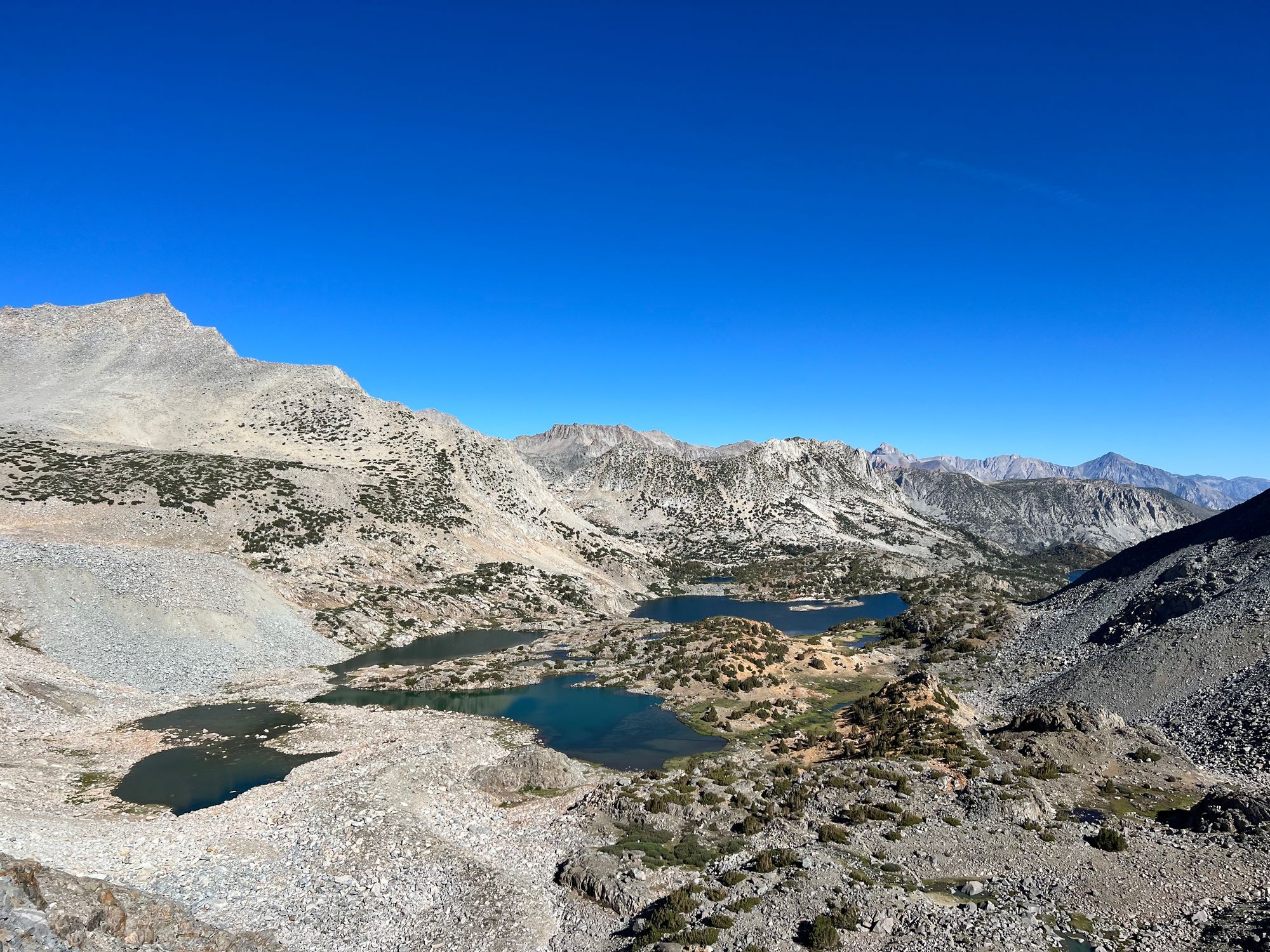 Several lakes on the bottom of a rocky valley dotted with stands of pine trees.