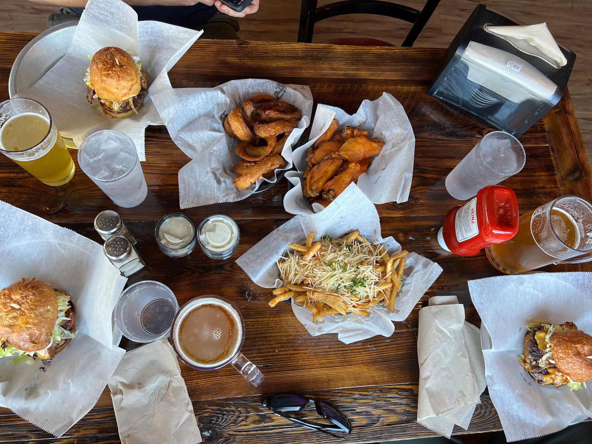 A table with 3 hamburgers, a basket of fries, onion rings, and chicken wings.