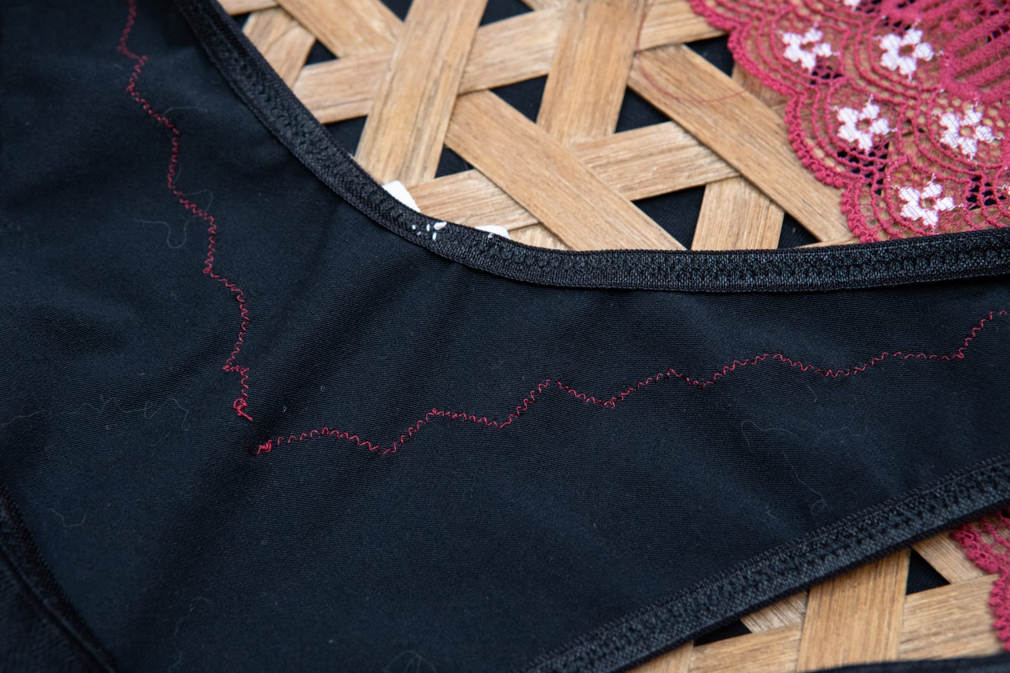 red thread is used to sew a small zigzag stitch over red lace. The inside of the underwear is black