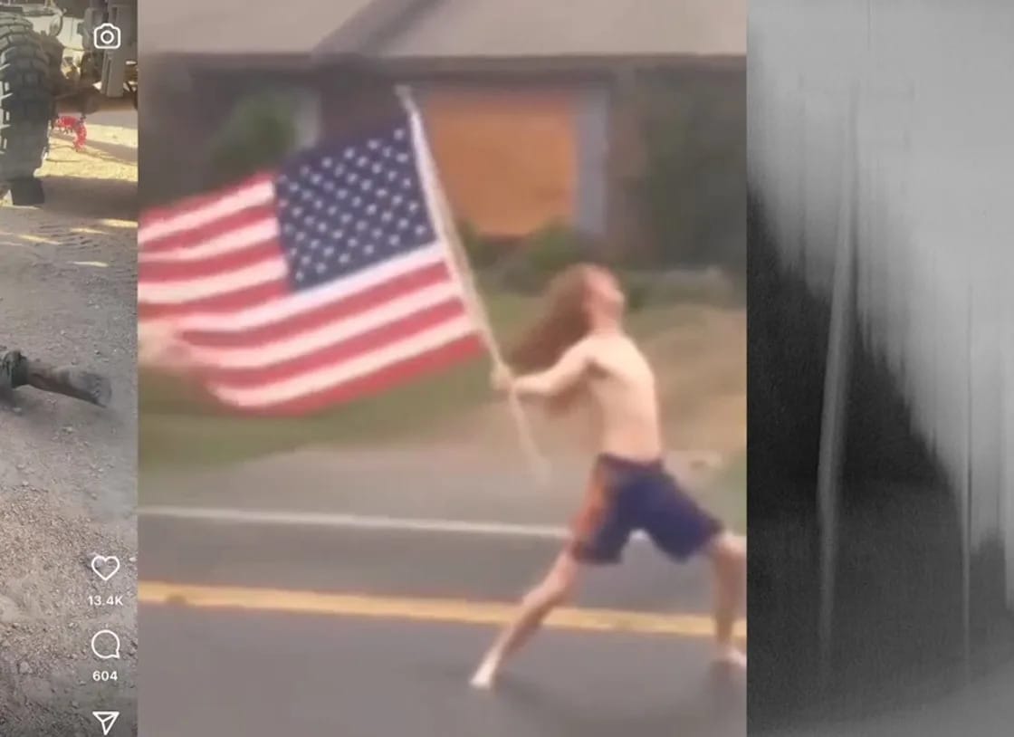 Blurred view of a shirtless white man in shorts with long hair walking down a street holding a large US flag.