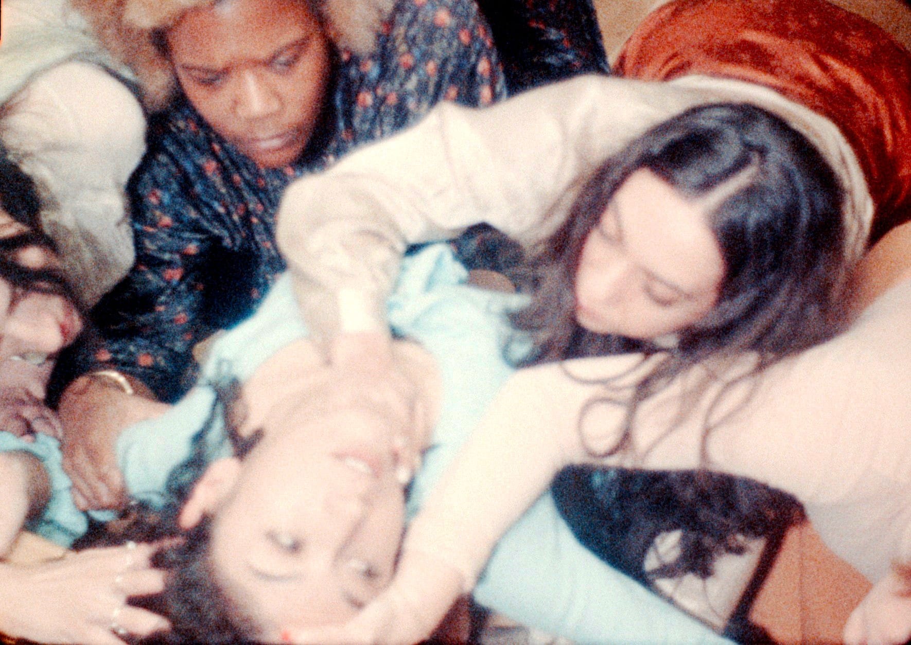 A blurry film frame with five figures embracing each other, with a man in the middle being held by his arms and with a hand around his neck.