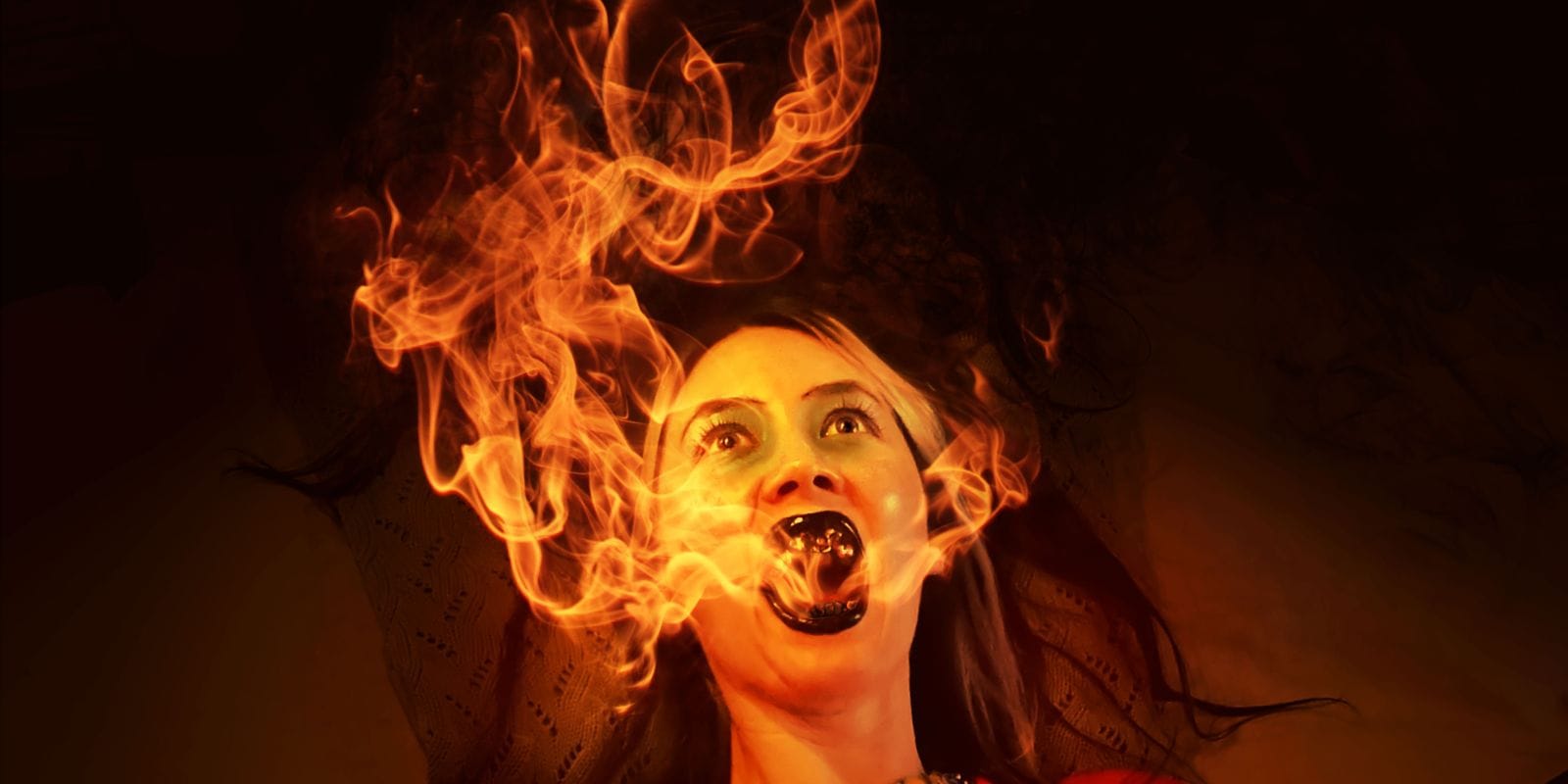 A woman with black lipstick with flames and smoke coming out of her mouth.