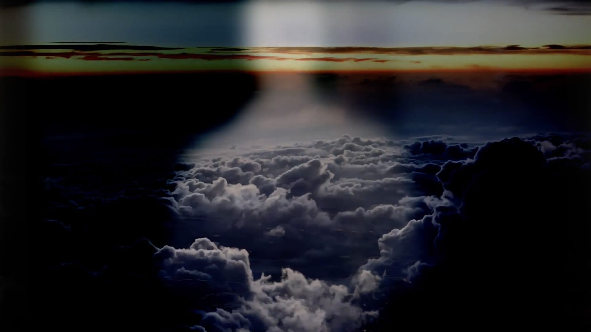 A dark image of a sky with clouds and a sunset on the horizon in the background.