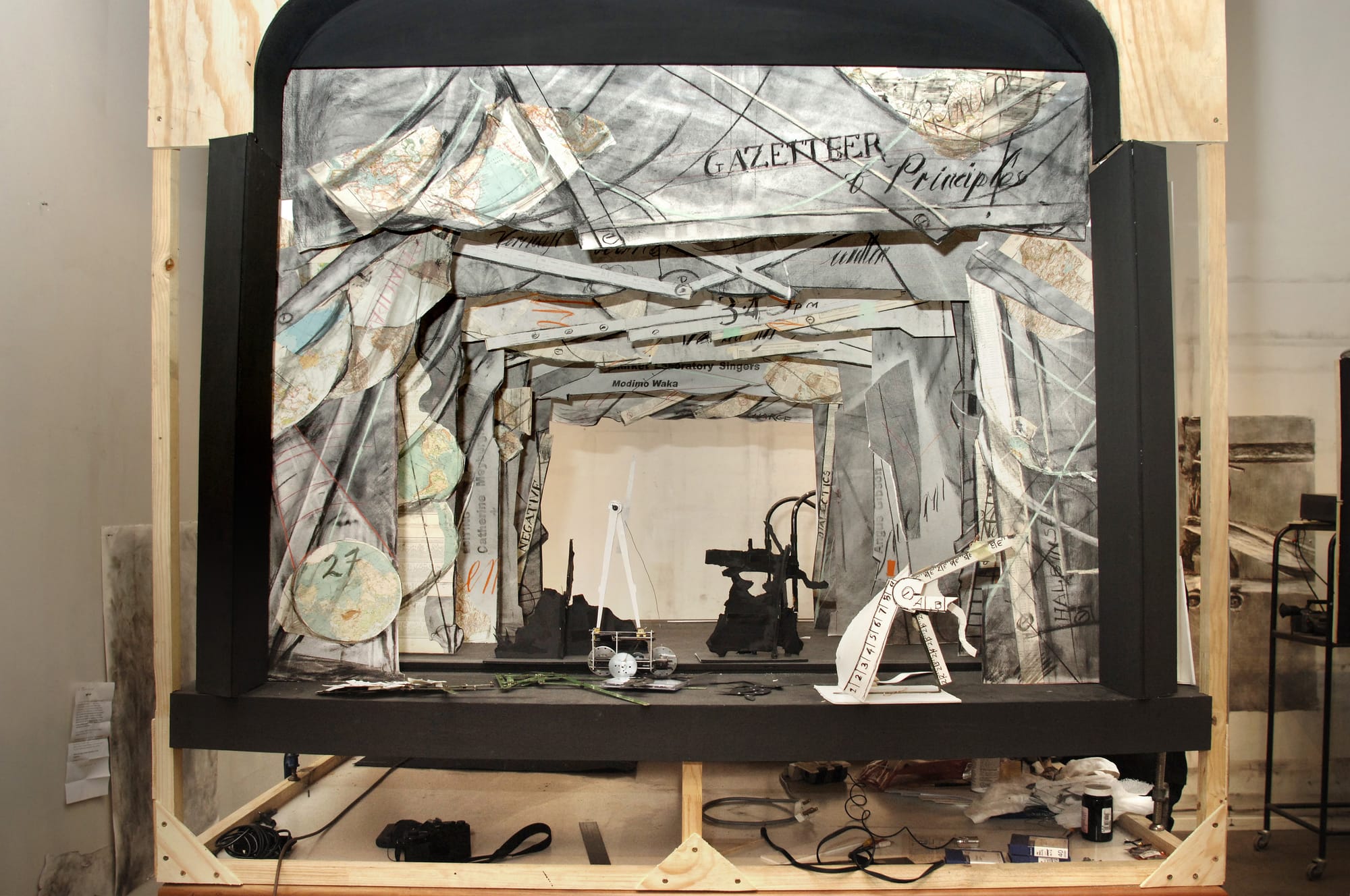 A small stage crafted out of wood, with newspaper curtains and mechanical objects as props.