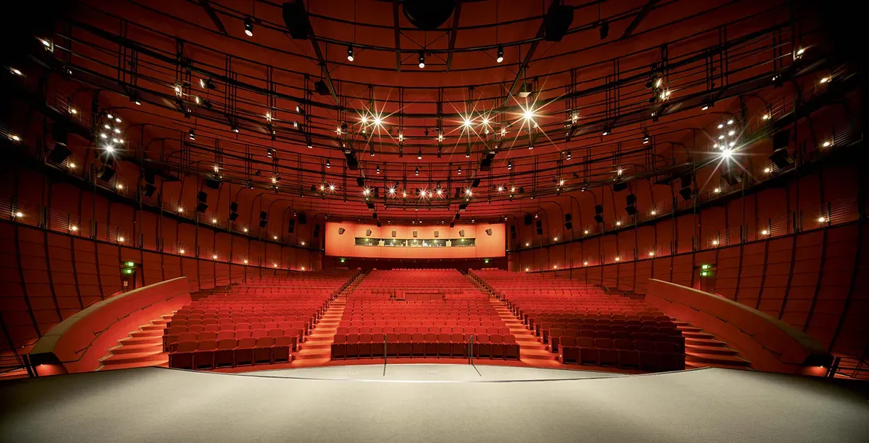 A spherical image of the interior of a large cinema screening hall, with red plush seats, red stairs and a wide array of lighting on the ceiling and walls.