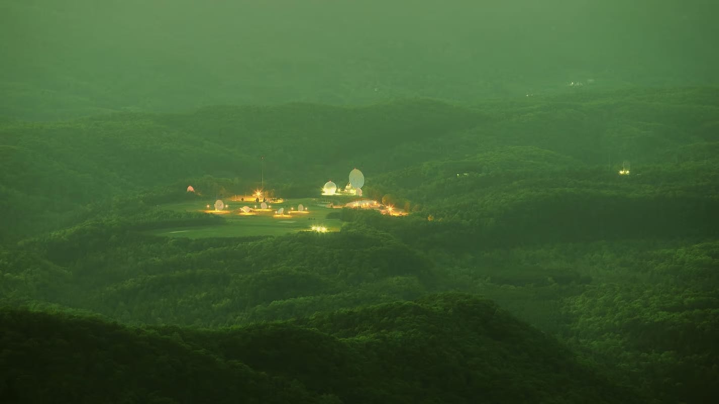 An image of rolling, lush green hills, with a group of satellites lit up in the distance.