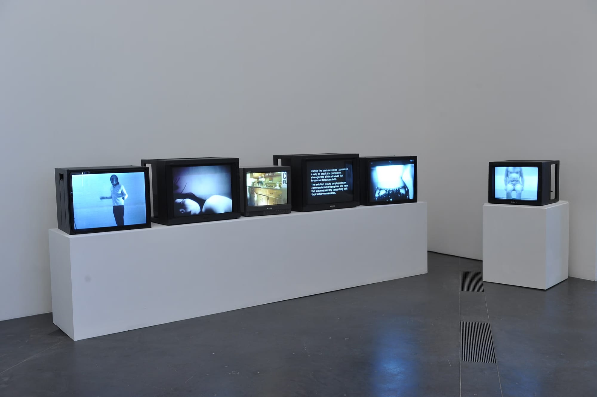 A gallery with six monitors sitting atop pedestals, each one showing an early video art piece.